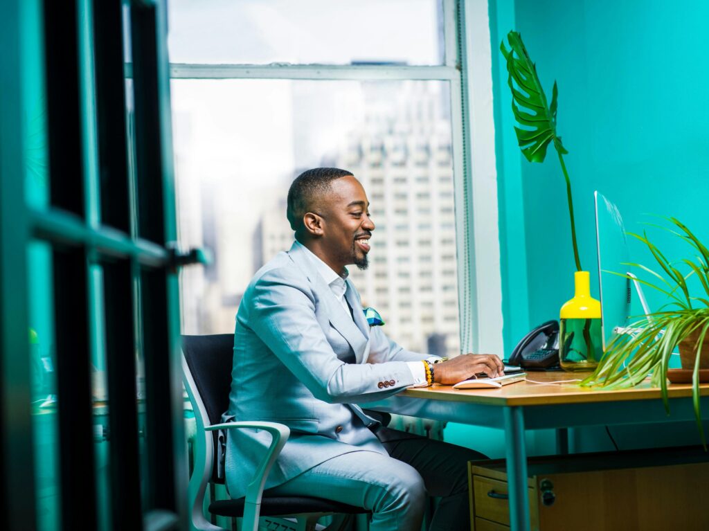 Confident businessman in modern office working on laptop with city view.